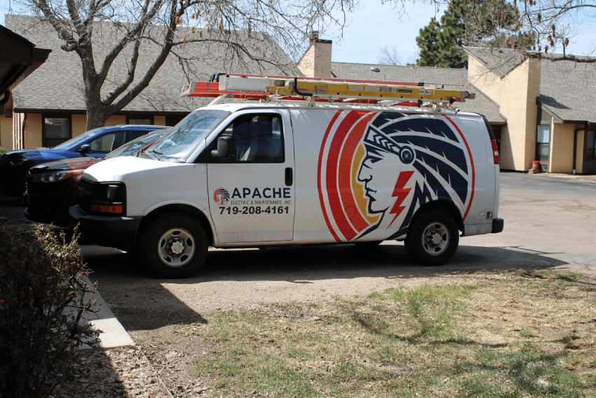 A white Apache electrical services van with a ladder on top is parked in a residential area; the logo features a stylized Native American profile.